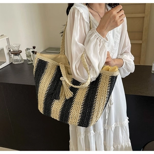 Detail of woven straw tote bag with black and yellow stripes and decorative tassels
