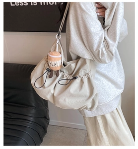 Close-up of beige drawstring shoulder bag with pleated texture and plush cup charm