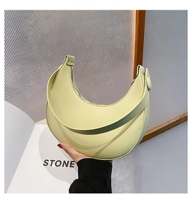 Detail of the light green moon-shaped PU leather bag featuring a smooth curved zipper and wide strap