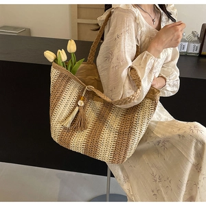 Close-up of woven straw tote bag featuring decorative tassels and beaded charm detail