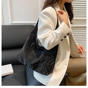 Détail du grand sac cabas noir à texture plissée porté avec un élégant tailleur blanc