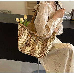 Detail of woven straw tote bag with horizontal stripes and shell fringe charm