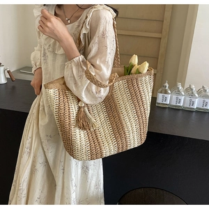 Detail of woven straw tote bag with brown stripes, tassel, and pearl charm detail