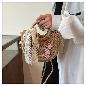 Détail d'un sac demi-lune en paille beige avec broderie florale et ruban en dentelle