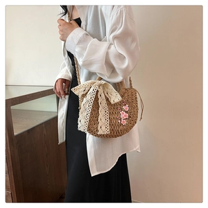 Détail d'un sac en paille tissée avec broderie cerisier rose et nœud en dentelle blanche