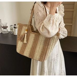 Detail of woven straw tote bag with brown stripes and tassel charm on summer dress