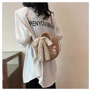 Détail du sac en paille tissée avec nœud en dentelle blanche et broderie florale rose