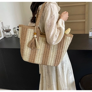 Detail of woven straw tote bag with beige and brown stripes and a decorative tassel charm