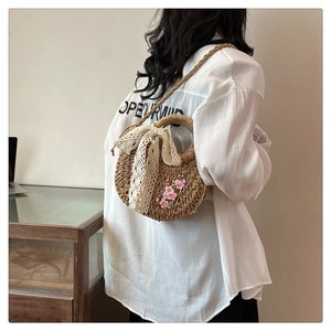 Détail d'un sac bandoulière en paille tressée avec broderie cerisier et nœud en dentelle