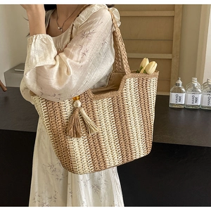 Detail of hand-woven straw tote bag with beaded tassel charm and woven top handles