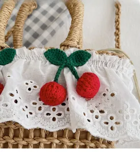 Detail of straw woven handbag with white lace trim and handmade crochet cherry accents