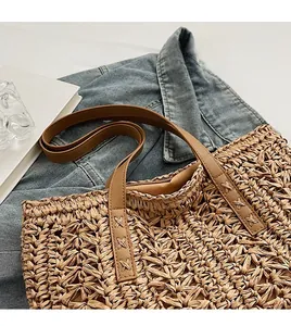 Detail of straw woven tote bag featuring brown leather straps and X-shape stitching