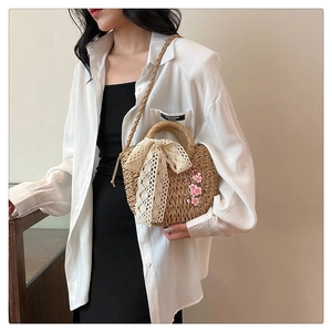 Détail du sac en paille tressée avec nœud en dentelle délicate et broderies de fleurs roses