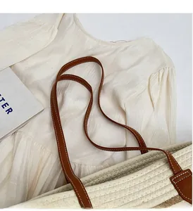 Close-up of beige woven tote bag with brown leather handles and decorative white stitching