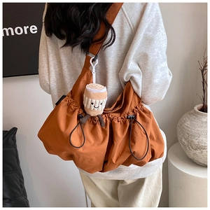 Close-up of canvas crossbody bag in orange-brown with drawstring and coffee plush charm