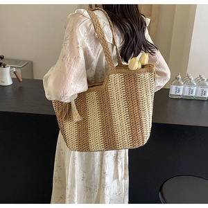 Detail of woven straw tote bag with brown stripes and decorative tassel in a summer style