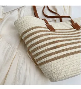 Detail of woven straw tote bag with brown stripes and leather strap on white fabric