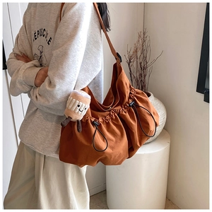 Detail of caramel orange pleated nylon tote bag with a cute plush charm on the strap