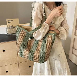 Detailed texture of green and beige woven straw tote bag with decorative tassels