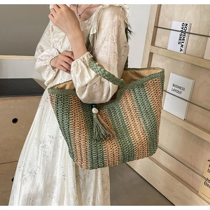 Close-up of woven straw tote bag with green stripes and decorative wood bead tassel