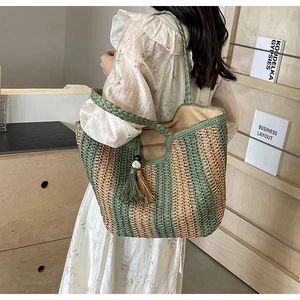Detail of woven straw tote bag with green stripes and decorative tassel on a model