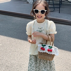 Detail of child's straw tote bag with lace trim and red cherry decor in a summer outfit