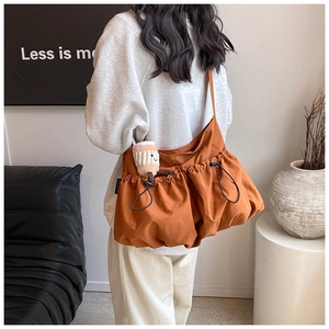 Detail of a large orange nylon crossbody bag featuring drawstring pockets and a plush charm