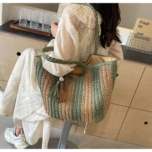 Detailed macro view of woven straw tote bag with green stripes and decorative tassel charm
