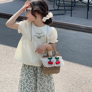 Detail of child wearing straw bag with lace trim and cherry decor in summer outfit
