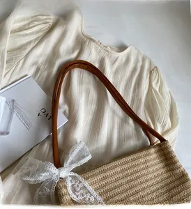 Vue détaillée du sac en paille tressée avec nœud en dentelle blanche et anses en cuir
