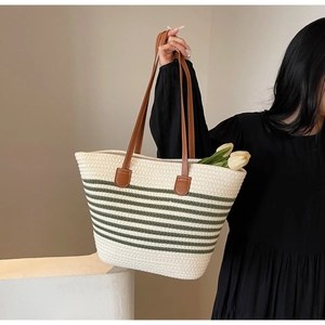 Detailed close-up of woven straw tote bag with green stripes and brown leather handles