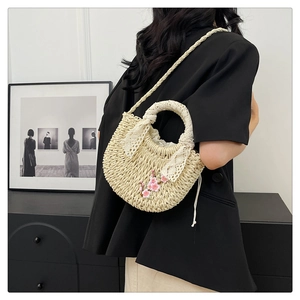 Détail d'un sac à main en paille tressée avec broderie florale rose et dentelle