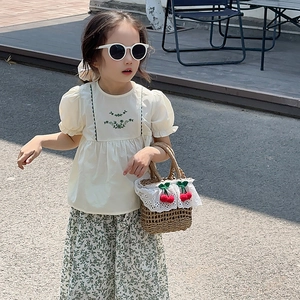 Detail of child wearing straw handbag with red cherry decor and floral summer outfit