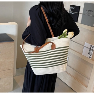 Close-up of woven tote bag featuring green stripes and brown leather shoulder straps