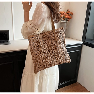 Detail view of woven straw tote bag featuring brown leather strap and reinforced stitching