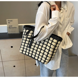 Détail du sac cabas en paille tissée à carreaux avec anses en cuir sur un modèle