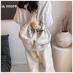 Minimalist beige drawstring crossbody bag shown on a model with a coffee plush charm
