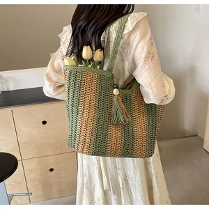 Close-up of woven straw tote bag with green stripes, wooden beads, and fringe details