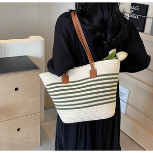 Detail of woven tote bag with green stripes and brown leather straps in a home setting