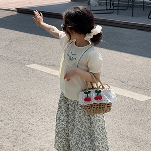 Close-up of girls' summer outfit featuring green botanical embroidery on a beige blouse