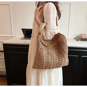 Detail of hand-woven straw shoulder bag with brown leather strap worn by a model