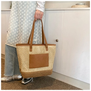Detail of straw woven tote bag featuring brown leather trim and decorative front pocket