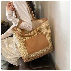 Detail view of woven straw tote bag with brown leather pocket and long shoulder straps
