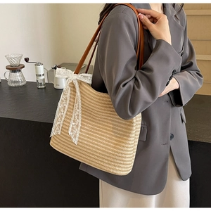 Détail d'un grand sac cabas en paille avec nœuds en dentelle blanche et anses en cuir marron