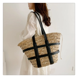 Detail of hand-woven straw tote bag with black leather straps and drawstring closure