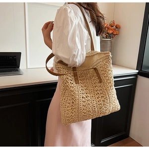 Detail of handwoven straw tote bag with brown leather handles worn by a model