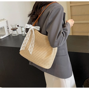 Détail du sac cabas en paille tissée avec bandoulière en cuir brun et nœud en dentelle