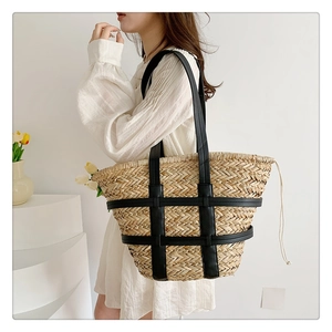 Detail of woven straw tote bag featuring black leather straps and drawstring closure