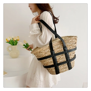 Detail view of the hand-woven straw tote bag with black leather straps on a model