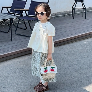 Close-up of a child straw handbag with detailed 3D cherry accents in a summer setting